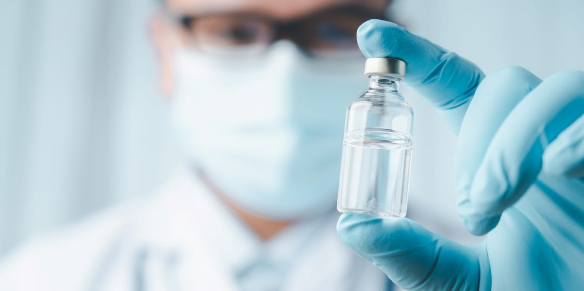 A doctor wearing a mask holds a vial with vaccine