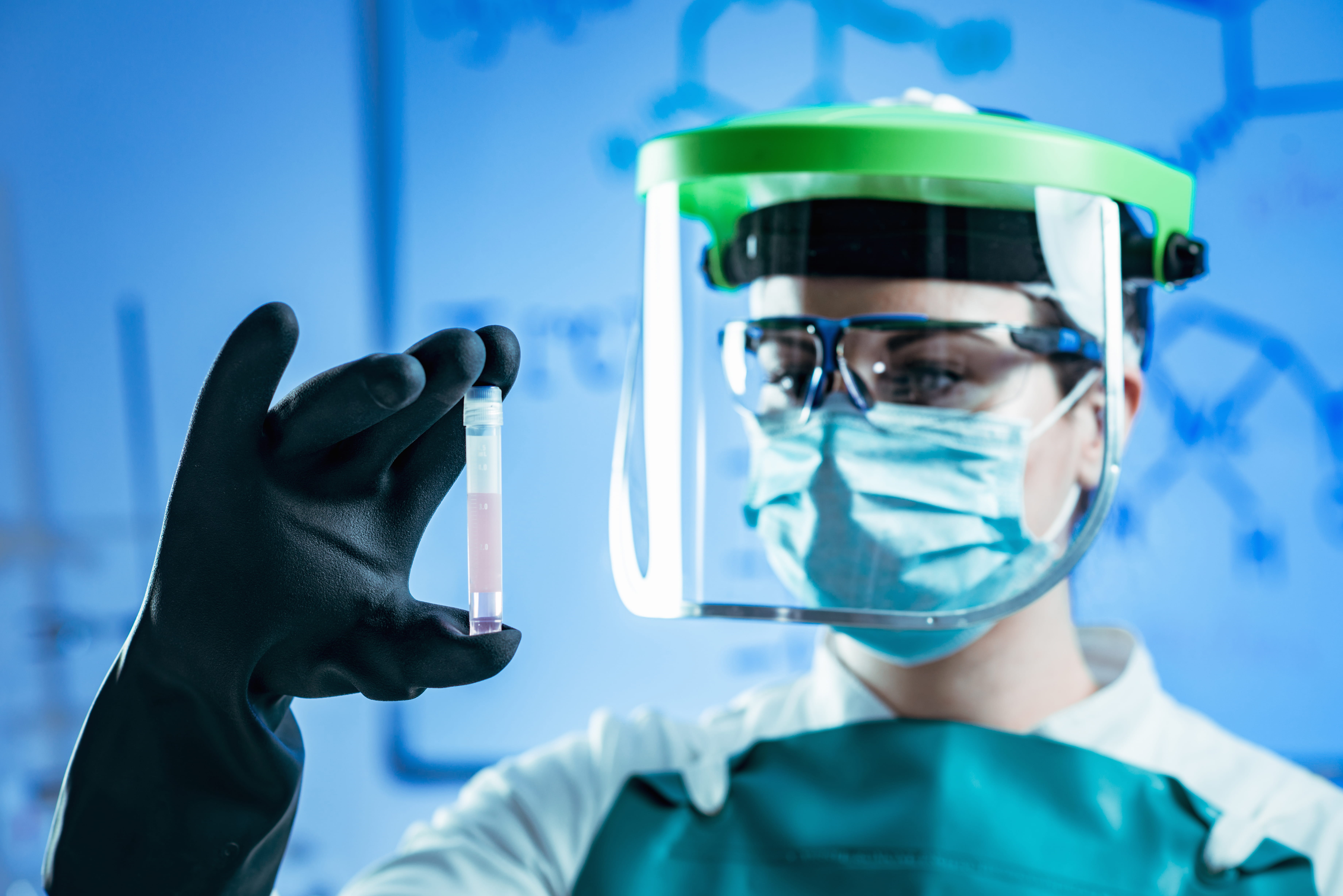 A scientist wearing a mask is examining a vial