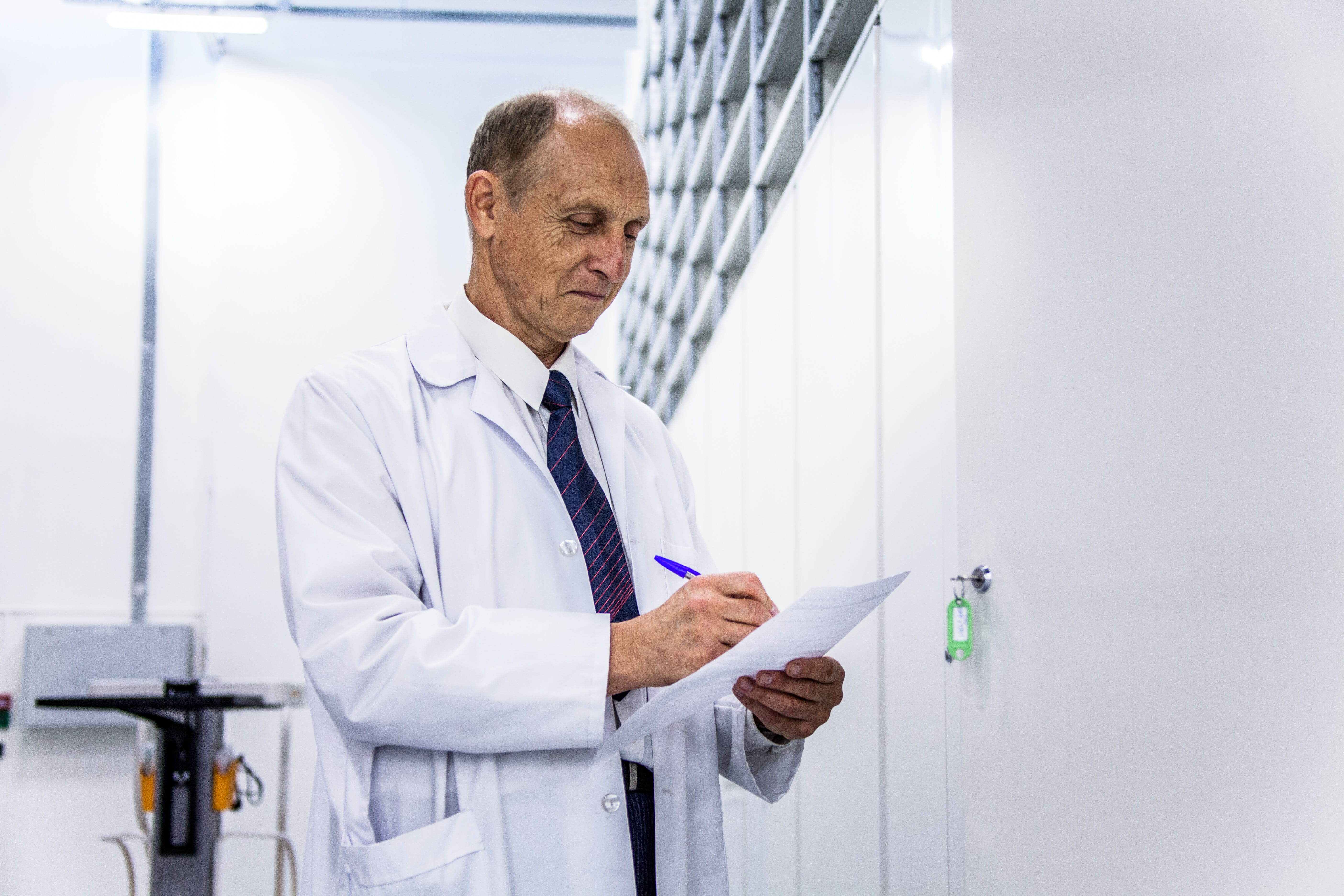 A man in a lab coat writes notes on a piece of paper standing in a pharmaceutical storage depot.