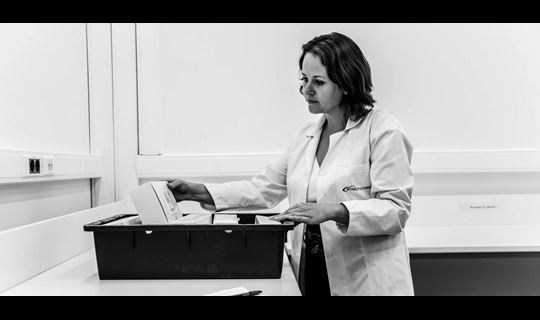 A woman in a lab coat looking at storage container with medication in it.