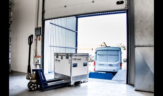 A shipping container is prepared to be loaded into a van at a loading dock.